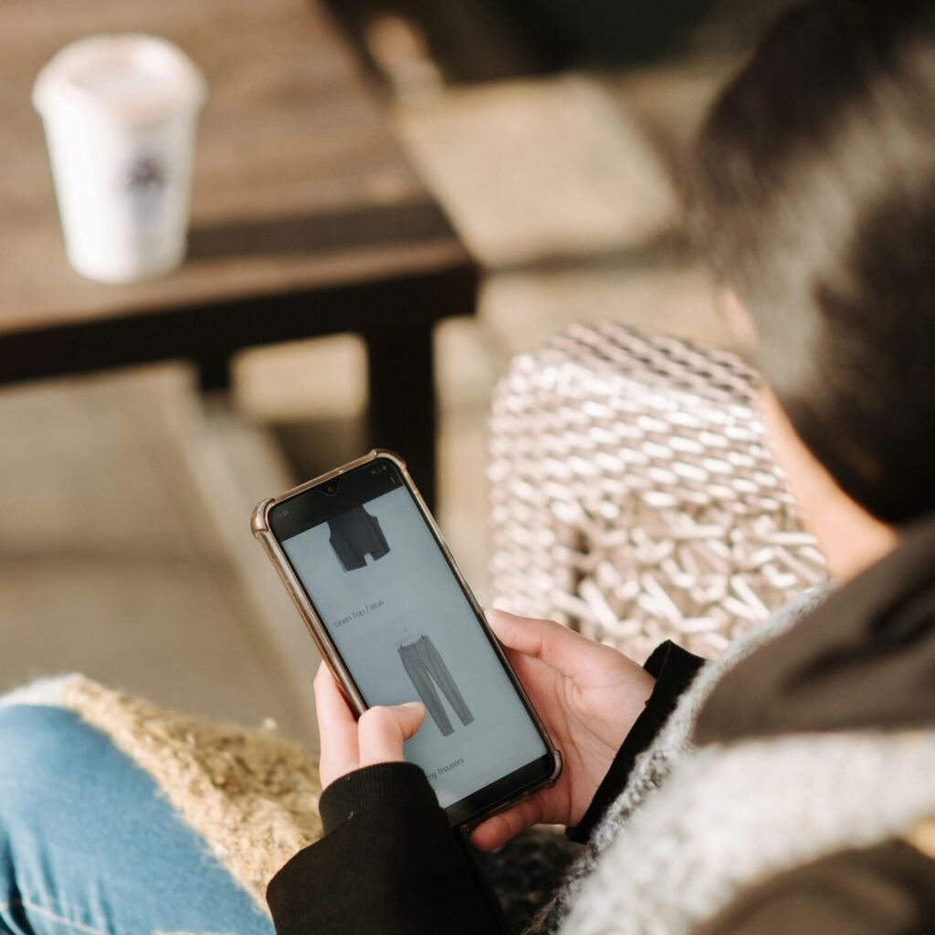 Unrecognizable woman in warm clothes using mobile phone for online shopping sitting in cafe